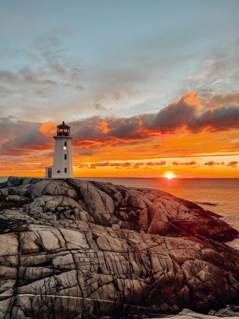 Peggy's Cove vuurtoren met zonsondergang en rotsachtige kust
