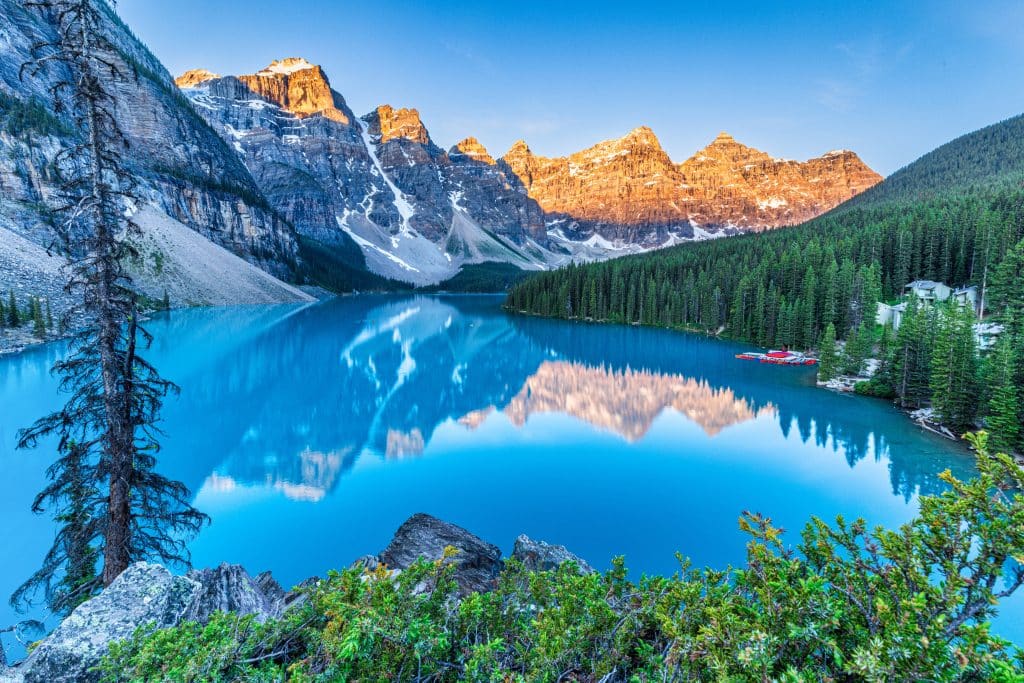 Heldere ochtend bij Moraine Lake met blauwe kleur en bergtoppen die zich spiegelen in het water.