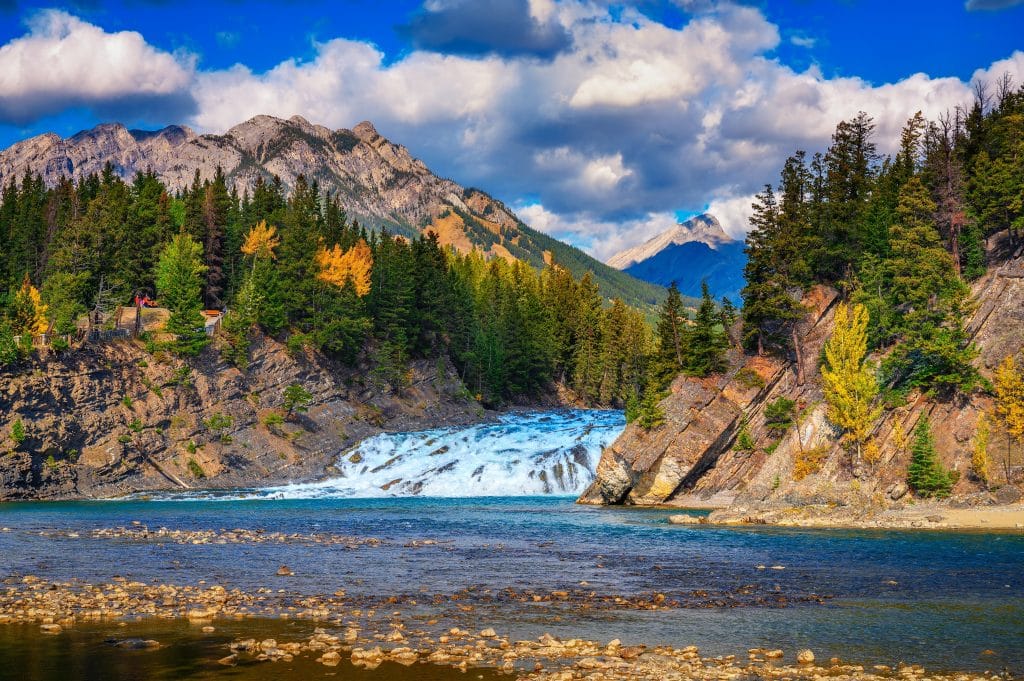 Waterval in Banff National Park met naaldbomen en bergen op de achtergrond.