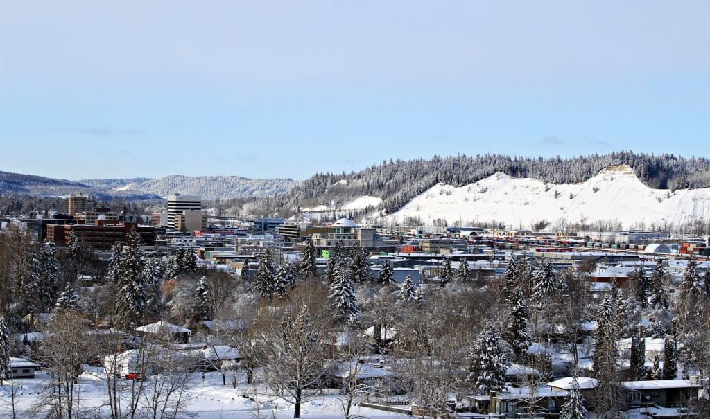 Winterzicht op Prince George met besneeuwde huizen, bomen en omliggende heuvels.
