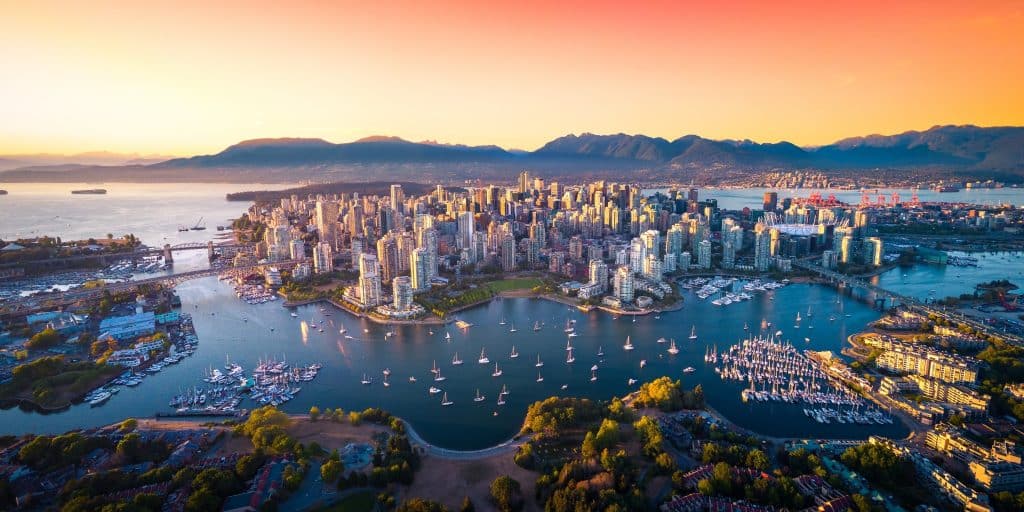 Luchtfoto van Vancouver met de jachthaven, hoge gebouwen en omringende bergen bij zacht avondlicht.