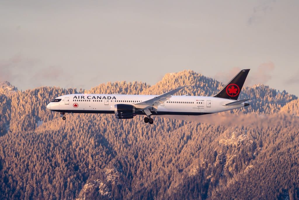Air Canada Boeing 787 Dreamliner vliegt boven besneeuwde bergen bij zonsondergang