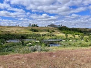 Wanuskewin Heritage Park met bezoekerscentrum, kreek, voetbrug en prairie.